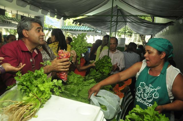 Consumidor e agricultora conversam sobre produtos em frente à banca de verduras