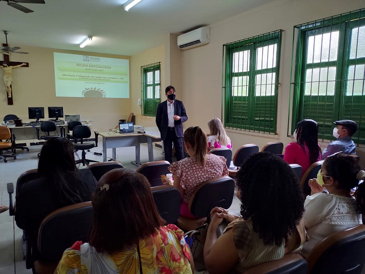 Sala de aula composta por alunos e um palestrante ao fundo 