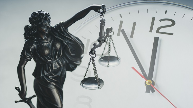 Na foto, um símbolo da Justiça próximo a um relógio