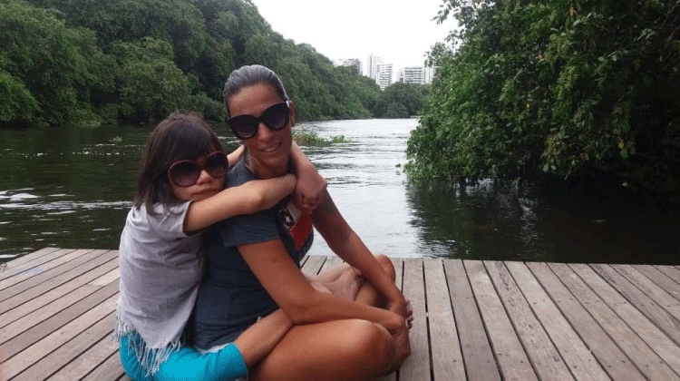 A afilhada Jaise abraçada à madrinha Rita Falcão. Ao fundo da imagem um rio
