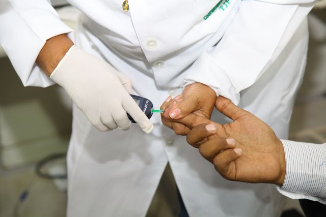 Enferemeira segura dedo do paciente, para fazer exame de glicose