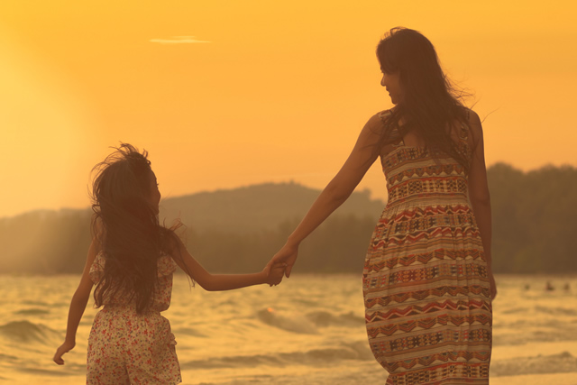 Mãe e filha caminham de mãos dadas na praia
