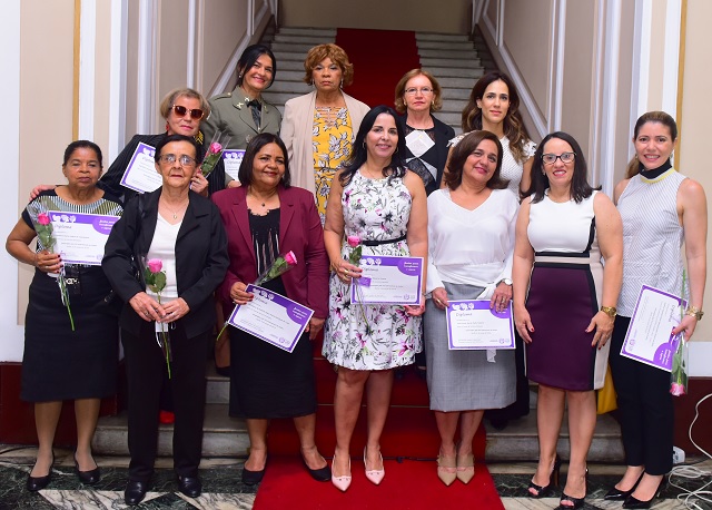 Doze mulheres lado a lado segurando diplomas de honra ao mérito