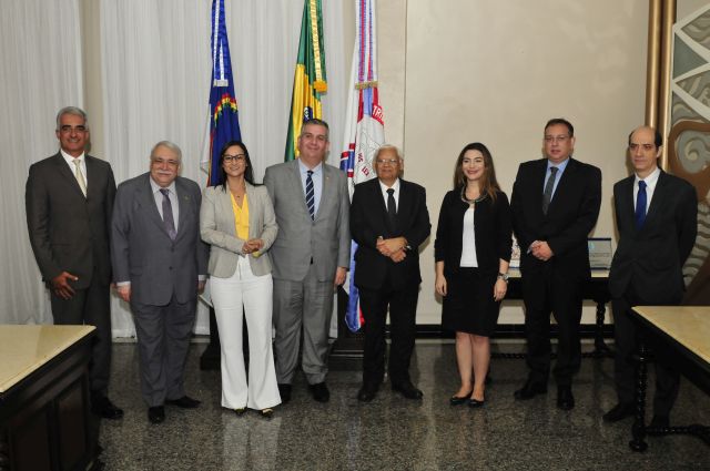Oito representantes da OAB-PE e do TJPE posando lado a lado  com bandeiras ao fundo da imagem