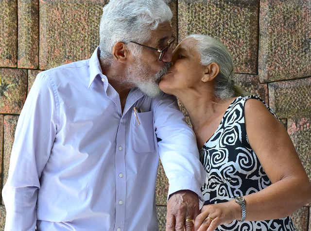 Homem e mulher, um casal de idoso, se beijam e mostram as alianças nos dedos