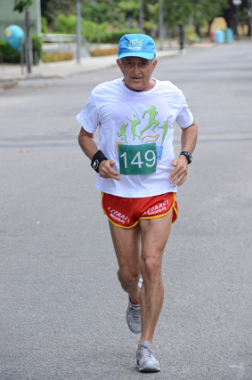 Desembargador correndo no meio da rua, usando camisa branca  e calção e boné vermelhos, chegando ao final da corrida