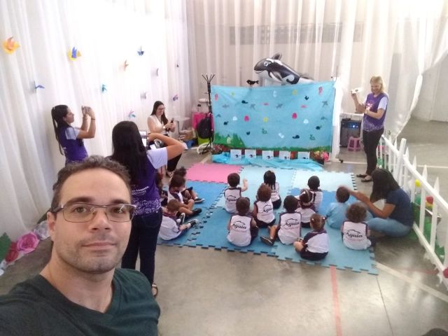 Servidor tira selfie em sala que mostra crianças e recreadoras em um colégio