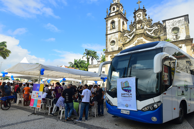 Ônibus do TJPE estacionado no Pátio do Carmo, com a igreja ao fundo, e estrutura montada ao lado do ônibus com pessoas sendo atendidas
