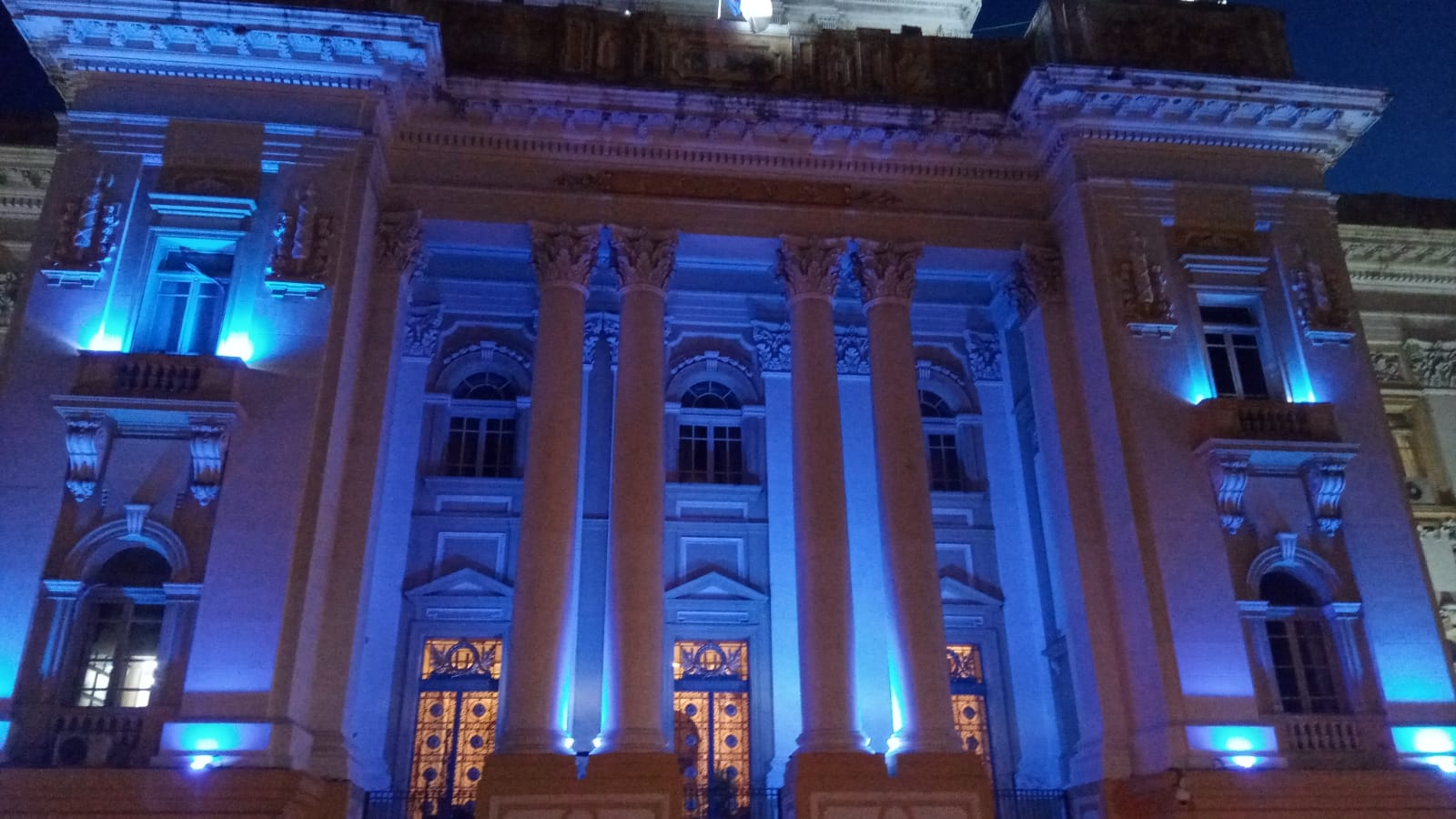 Foto exibe fachada do prédio do Palácio da Justiça iluminada na cor azul