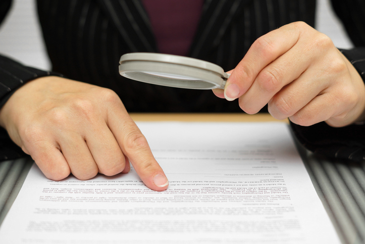 Foto de uma pessoa lendo um contrato com uma lupa com destaque para as mãos sobre o documento