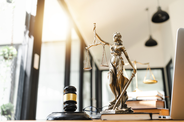 Imagem da Deusa da Justiça Themis em cima de uma mesa ao lado de um martelo judicial