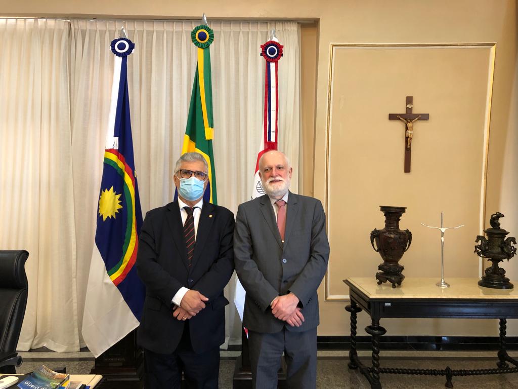 Foto mostra dois homens de pé, um ao lado do outro. Ao fundo aparecem as bandeiras do Brasil, de Pernambuco e do TJPE