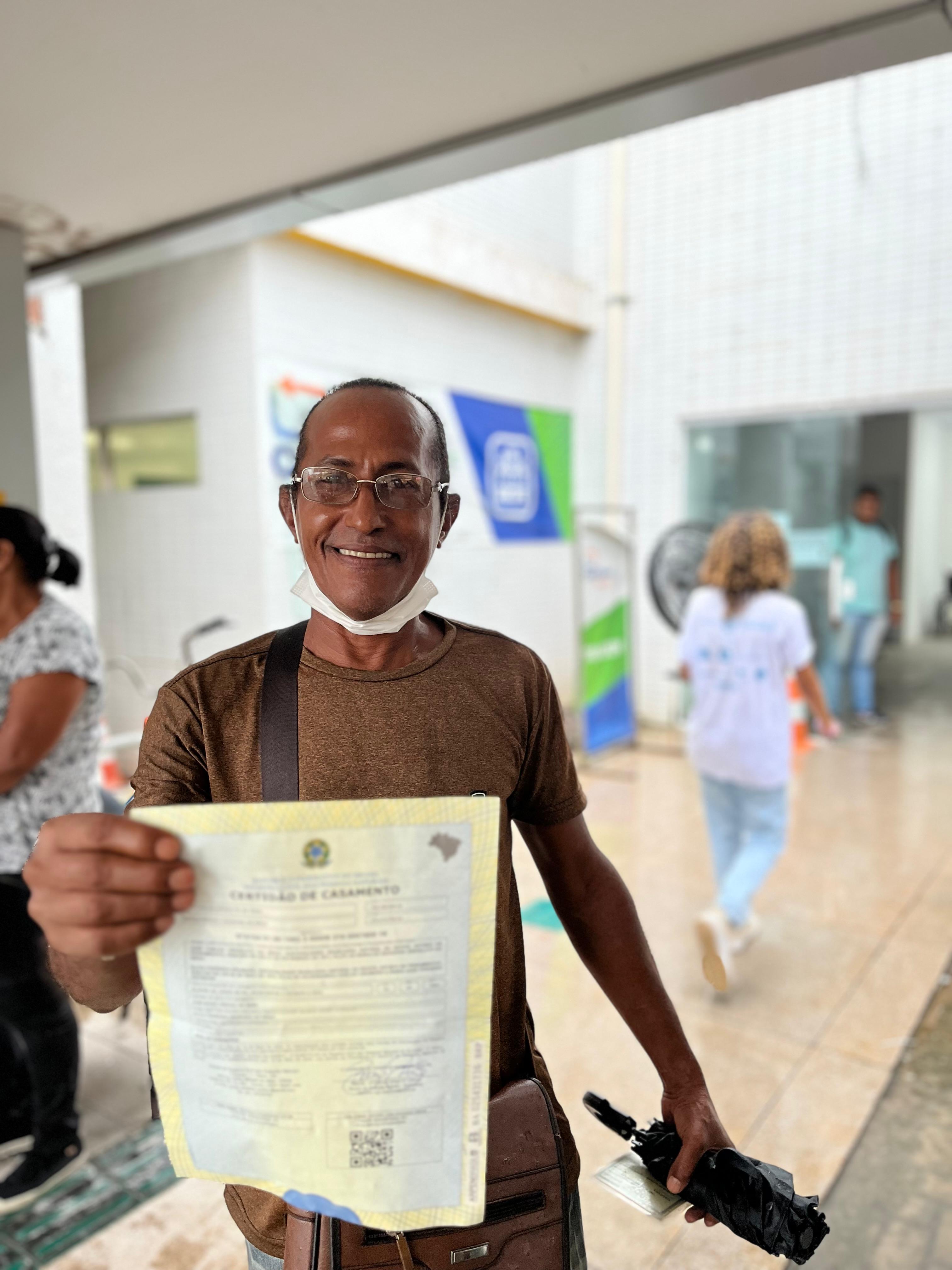 Foto mostra homem beneficiado durante a Semana Nacional do Registro Civil - Registre-se! segurando sua certidão. 