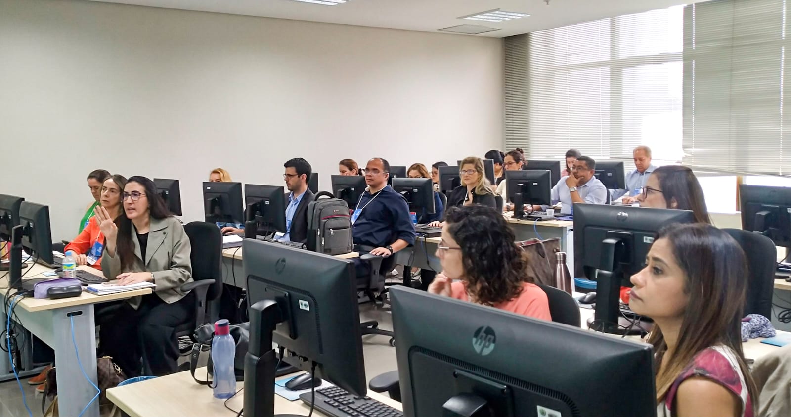 Laboratório de informática cheio de computadores e servidores e servidoras sentados usando-os durante capacitação