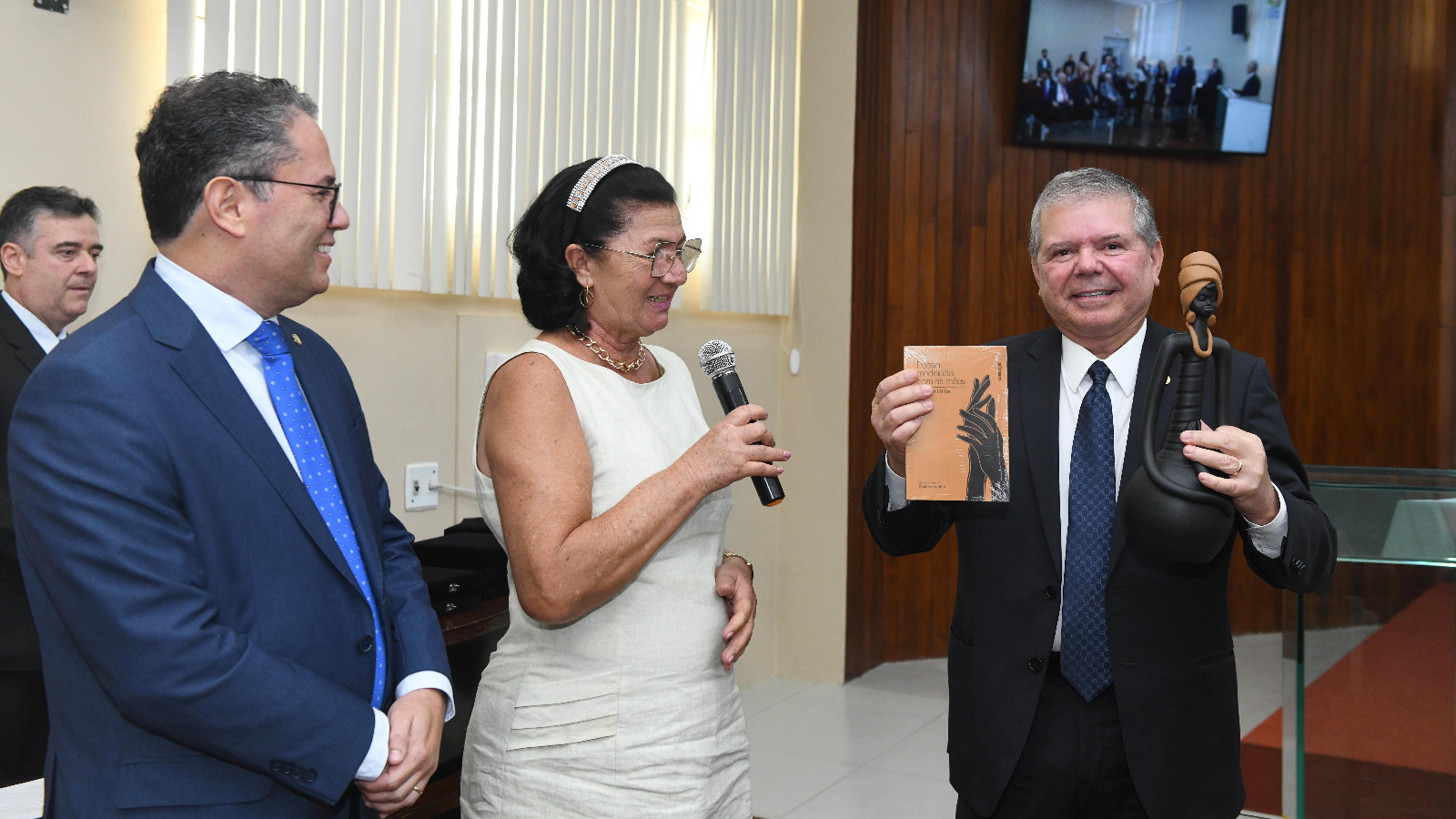 Presidente do TJPE segura um livro e uma escultura de uma mulher negra com turbante amarelo sentada em meditação de cerca de 40cm de altura.