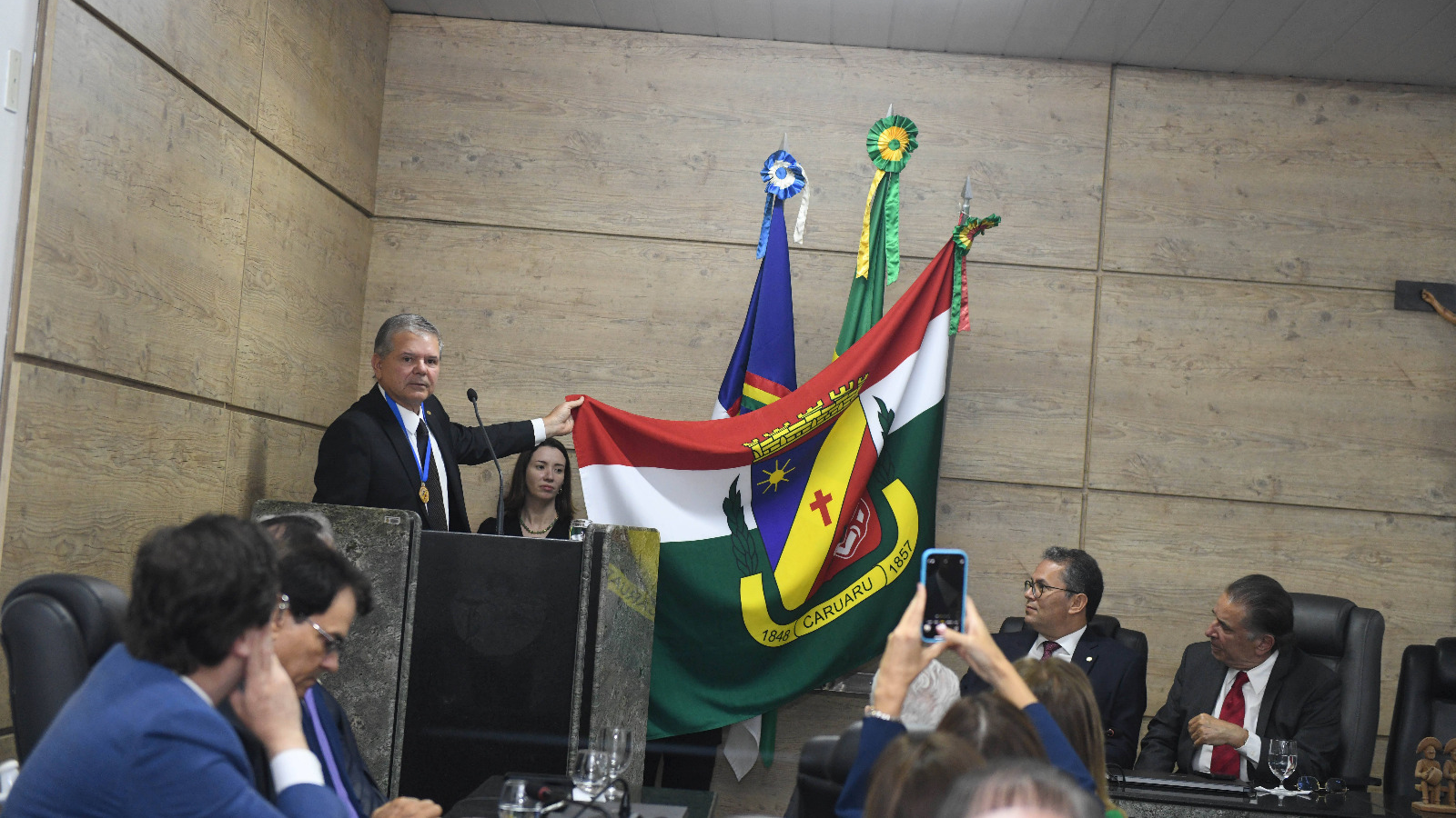 Presidente do TJPE, no púlpito, estendendo a bandeira de Caruaru que estava no mastro de enfeite.