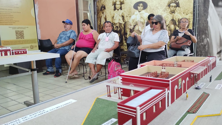 Em primeiro plano, maquete tátil do Memorial da Justiça de Pernambuco. Ao fundo, pessoas com deficiência visual aguardam para conhecer o museu.