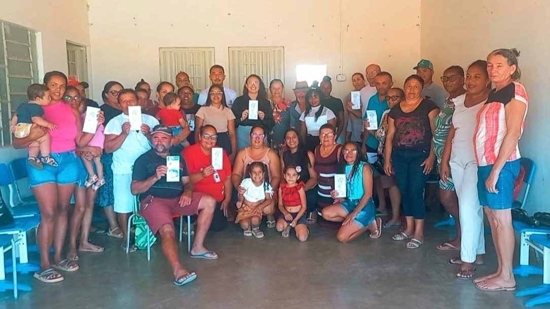 Diversas pessoas da comunidade quilombola juntas mostrando os cartões informativos em um espaço comunal fechado.