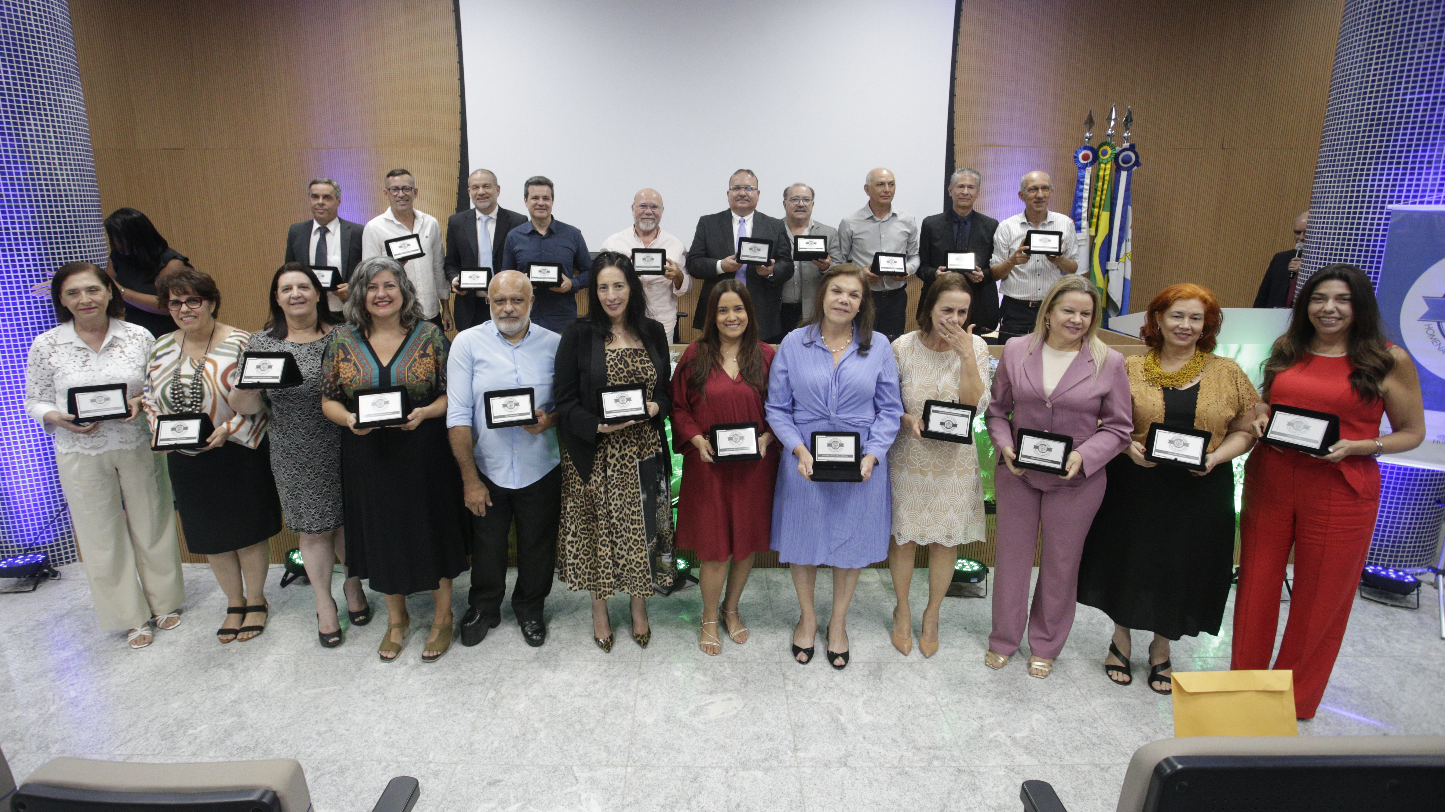 Servidores segurando suas placas comemorativas em frente ao palco.