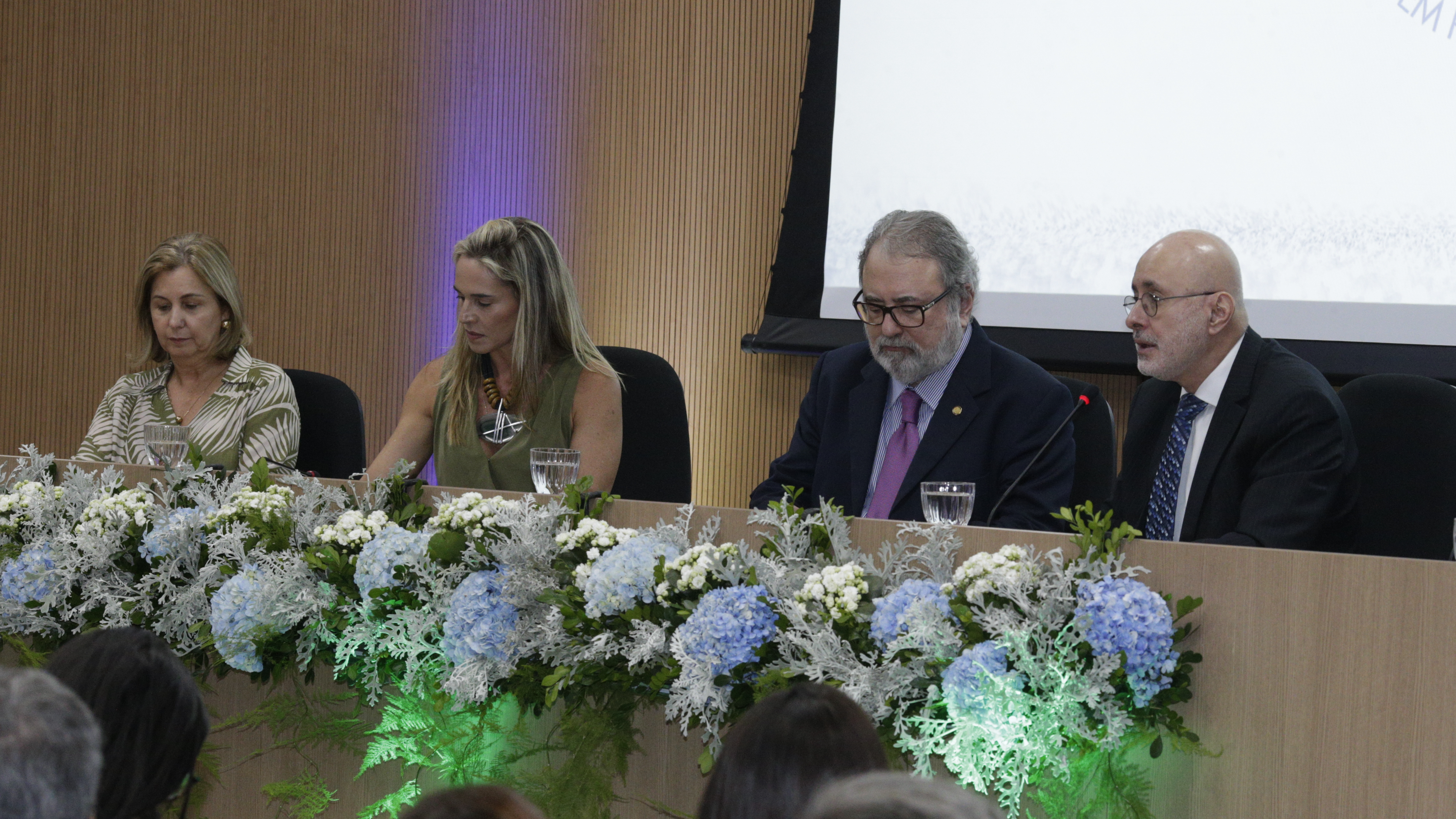 Desembargadores, vice-prefeita e diretora de desenvolvimento humano sentados à mesa no palco.