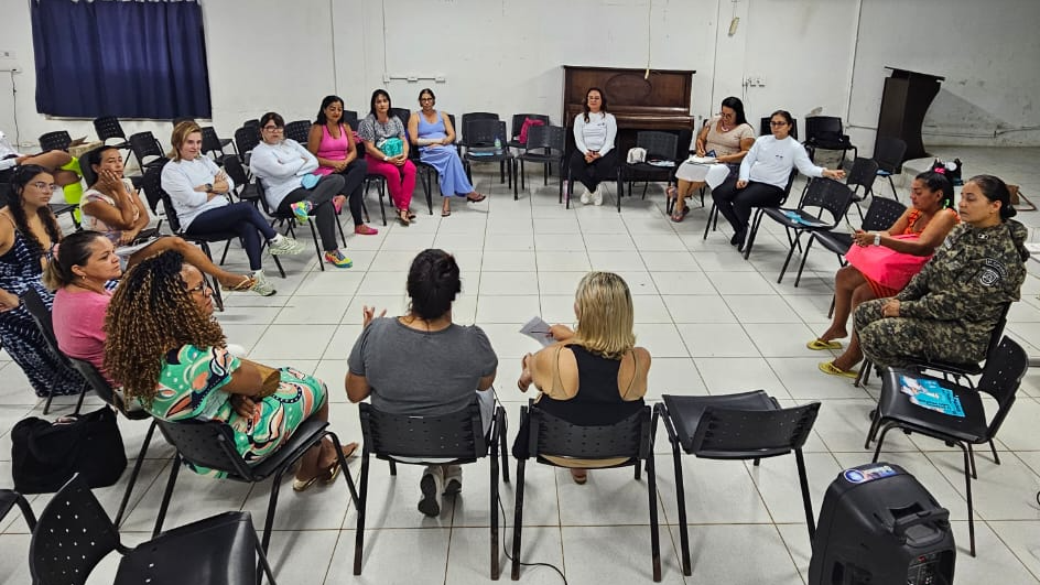 Diversas mulheres sentando-se em círculo em uma sala de aula com paredes brancas.