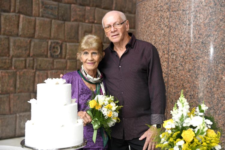 Rosa é uma mulher idosa, baixa, de cabelos e olhos claros, usando uma roupa roxa. Ela segura um buque de flores branco. Wellington é um homem idoso, careca, alto, olhos claros, pele branca e que usa óculos e uma camisa listrada preta.